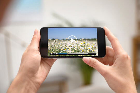 Woman watching video on mobile phone at home, closeup