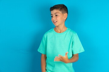 Little hispanic boy wearing green T-shirt smiling and looking friendly, showing number five or fifth with hand forward, counting down