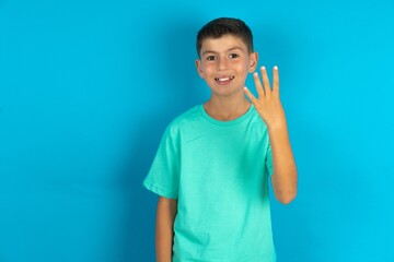 Little hispanic boy wearing green T-shirt smiling and looking friendly, showing number four or...