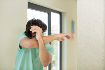 young crazy bearded man covering face with hand and putting other hand up front to stop camera,...