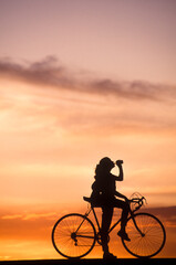 Fototapeta na wymiar Teenage girl on a bicycle having a drink at sunset