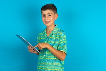Photo of happy cheerful smart Little hispanic boy wearing green aztec shirt hold tablet browsing internet