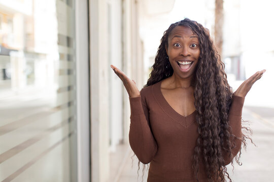 afro pretty black woman feeling happy, excited, surprised or shocked, smiling and astonished at something unbelievable