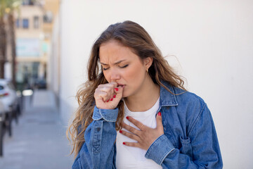 pretty hispanic woman feeling ill with a sore throat and flu symptoms, coughing with mouth covered - obrazy, fototapety, plakaty