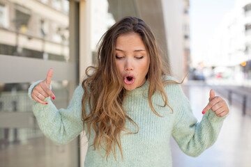 Fototapeta premium pretty hispanic woman with open mouth pointing downwards with both hands, looking shocked, amazed and surprised