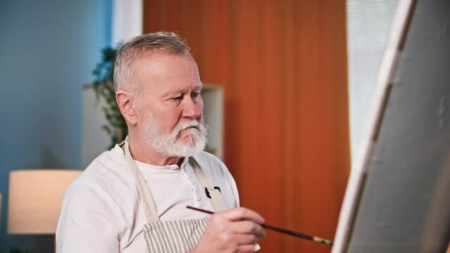 elderly retired man learning to paint pictures with brush and paint in room