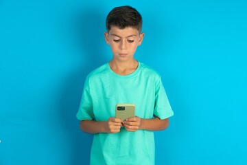 Focused Little hispanic boy wearing green T-shirt use smartphone reading social media news, or...