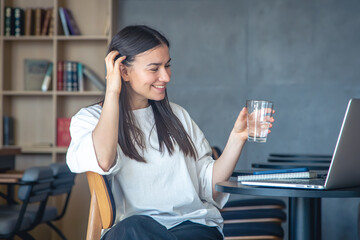 Young woman with a glass of water in front of a laptop.