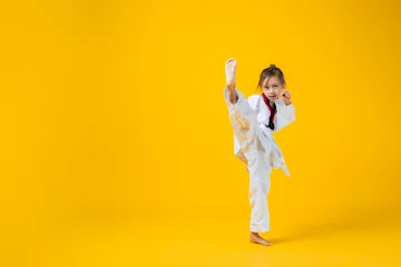 Foto op Plexiglas Banner: Asian-Australian girl poses in martial arts Practice taekwondo, karate, judo against a yellow background in the studio. Asian kids karate or Taekwondo martial arts. Sport kid training action. © VR Studio
