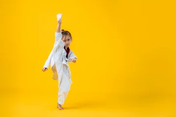 Fotobehang Banner: Asian-Australian girl poses in martial arts Practice taekwondo, karate, judo against a yellow background in the studio. Asian kids karate or Taekwondo martial arts. Sport kid training action. © VR Studio