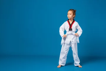 Tuinposter Banner: Asian-Australian girl poses in martial arts Practice taekwondo, karate, judo against a blue background in the studio. Asian kids karate or Taekwondo martial arts. Sport kid training action. © VR Studio