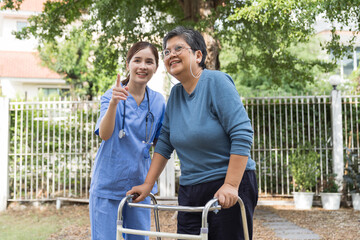 Nurse and patient senior woman with walker. Nurse caring senior woman walking with walker outdoor at hospital. Asian nurse taking care elderly woman with walker in garden at home