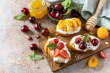 Sandwich with cherry, strawberries, soft cheese and honey on wooden board on a stone background. Berries toast breakfast, healthy food.  Copy space.