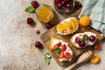 Fototapeta na wymiar Sandwich with cherry, strawberries, soft cheese and honey on wooden board on a stone background. Berries toast breakfast, healthy food. View from above. Copy space.
