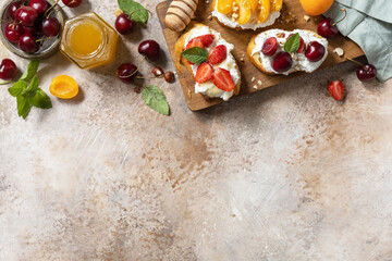 Fototapeta na wymiar Berries toast breakfast, healthy food. Sandwich with cherry, strawberries, soft cheese and honey on wooden board on a stone background. View from above. Copy space.