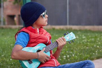 Pre-teen girl in casual clothes with a guitar in her hands is sitting with thoughtful expression deciding what song she is going to perform. Horizont composition and copy space in the upper right side