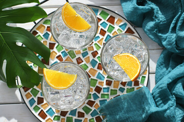 Spa water with orange slices or mixed drinks cocktails on boho mosaic tile tray, tropical greenery
