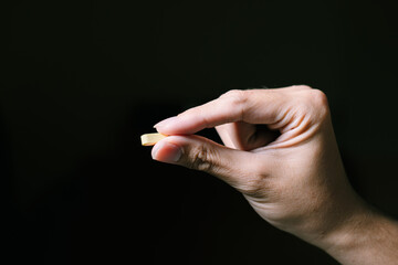 A yellow pill is held by pointing and thumb fingers. Isolated black background. Suitable for advertisement.