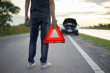 Close-up of male hands holding red emergency stop sign with broken down car on road.Red emergency stop sign with broken down car on the road waiting to be repaired.
