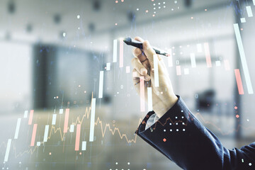 Man hand with pen working with abstract virtual financial graph on blurred office background, financial and trading concept. Multiexposure