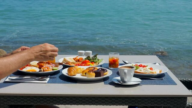 Tasty buffet breakfast served on table in luxury restaurant with sea view. Tropical summer vacation, holidays in modern resort. Man enjoys outside dining with fresh pastries.