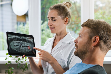 dentist showing and explaining dental x-ray picture with impacted wisdom tooth to his patient - 617109402