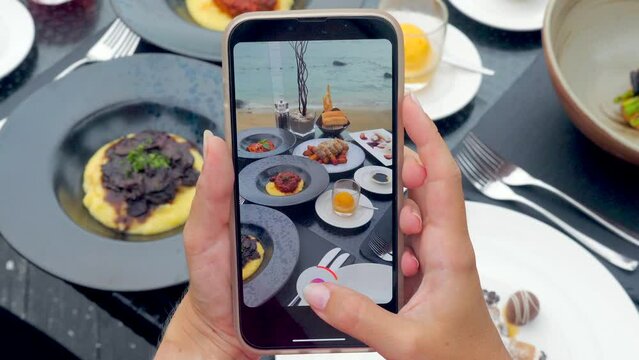 Closeup of a woman's hands using a smartphone to take photos of her dinner at an outdoor tropical restaurant. Captures the delicious meal with a trendy foodie app.