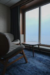 Living room with arm chairs and coffee table in front of panoramic windows with sea views inside...
