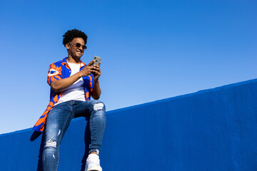 Smiling black man using smartphone and sitting on fence