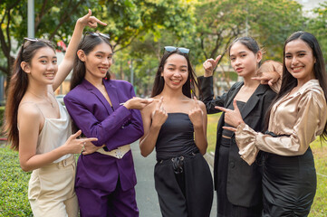 5 women point to their friend in the center as a sign of support, or endorsing their team leader. Outdoor scene at the park.