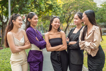 5 asian women, possibly workmates at the office, having a lighthearted discussion while taking a walk at the park.