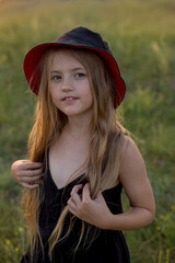 a beautiful and happy long-haired blonde girl in a black dress and a black panama hat stands in the...