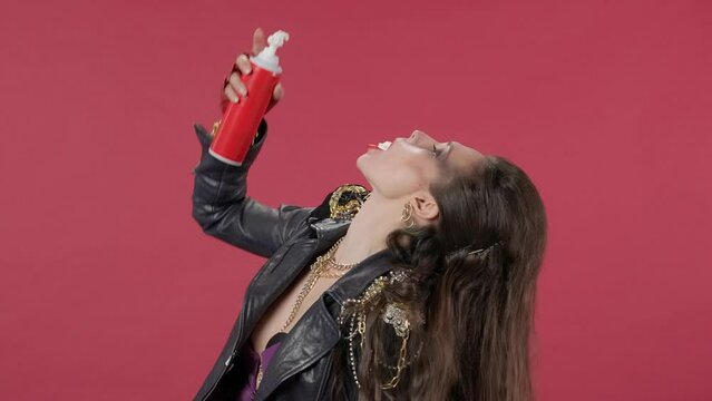 A woman shakes the can of whipped cream well, then squeezes the yummy into her mouth, winks. Portrait of a woman on a red background in the studio. Video 2 in 1. Advertising. HDR BT2020 HLG Material.