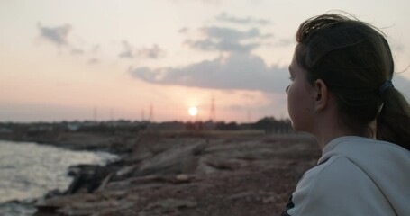 A teenage girl with her thoughts at sunset by the sea. Difficult teenage period of children, to be alone with nature to think. High quality 4k footage