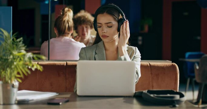 Adorable young woman in wireless earbuds headphones listens to music relaxes sitting at restaurant typing prepsres materials for job aplication interview .