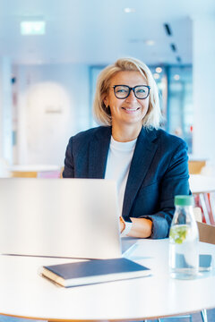 Portrait Of 50's Confident Mature Businesswoman Looking At Camera, Middle-aged Experienced Senior Female Professional Working On Laptop In Open Space Office. Female Entrepreneur Working Remotely.