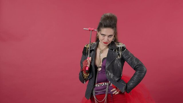 A woman takes a selfie on a smartphone using a monopod. Woman with bright makeup, fleece and in a leather jacket with chains in the studio on a red background. Advertising. HDR BT2020 HLG Material.