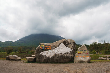 Rocks with sign of arenal 1968 trail and directional arrows in front of mountain volcano covered in...