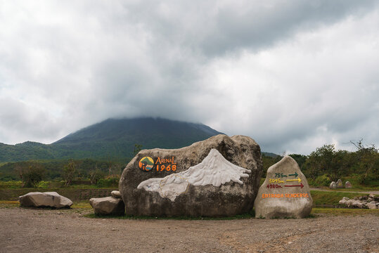 Rocks with sign of arenal 1968 trail and directional arrows in front of mountain volcano covered in clouds at Costa Rica