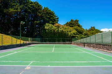 Empty outdoor tennis court with net and boundary fence surrounded with lush green trees at Costa Rica