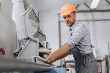 A male worker in a special uniform and an orange helmet works on a CNC machine for the production of PVC windows and doors at the factory.