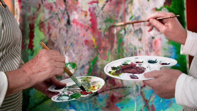 creative hobby, elderly artists paint a modern picture together with paints and brushes, close-up