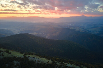 Aerial view of amazing scenery with foggy dark mountain peak covered with forest pine trees at autumn sunrise. Beautiful wild woodland with shining rays of light at dawn