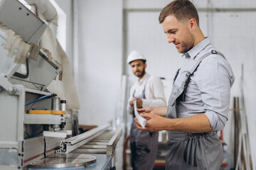 Obraz premium An international team, two workers work at a machine at a factory of PVC windows and doors