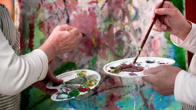 creativity in retirement, happy elderly spouses joyfully paint a modern picture together with paints and brushes on an easel, close-up