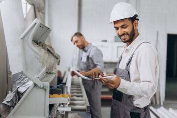 An international team, two workers work at a machine at a factory of PVC windows and doors