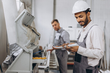An international team, two workers work at a machine at a factory of PVC windows and doors