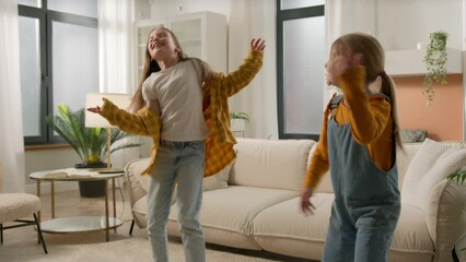 Happy satisfied active caucasian children sisters friends play together in living room have fun two funny playful carefree kids girls dancing jumping laughing celebrate enjoy game dance jump to music - Powered by Adobe