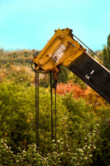 Obraz premium Construction crane weight lifting and lowering device among green trees. The crane looks like a dinosaur's head among the trees