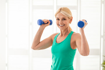 Home Training Concept. Sporty senior woman doing exercises with dumbbells indoors